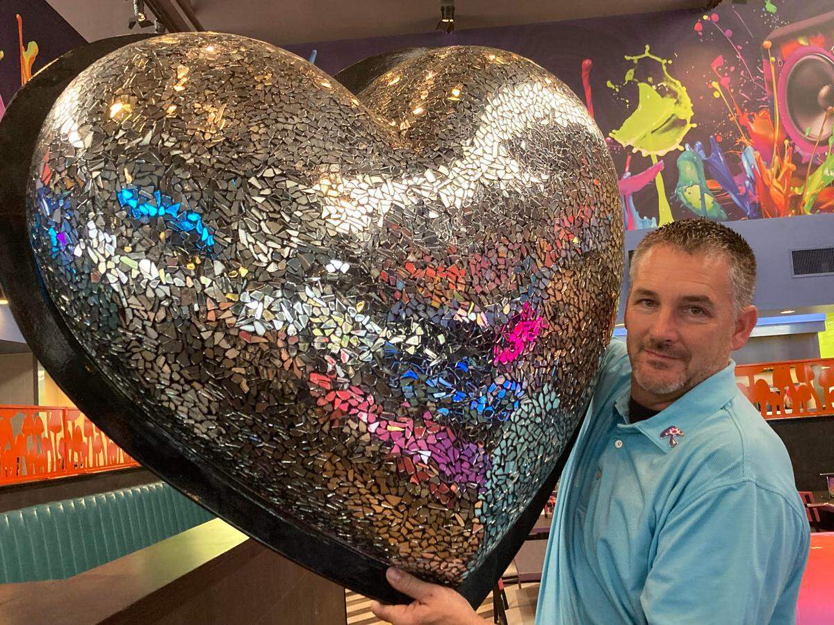 Brian Anderson holds up reflective heart to be mounted in Mellow Mushroom in Warner Robins as part of its remodel. He and his wife, Brittanie, are the franchise owners of the popular pizza spot.