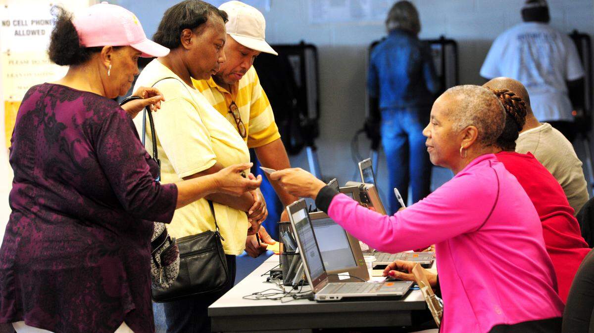 Election clerk Barbara White hands a voting ballot to an early voter in 2014 at the Bibb County Board of Elections Office in Macon.