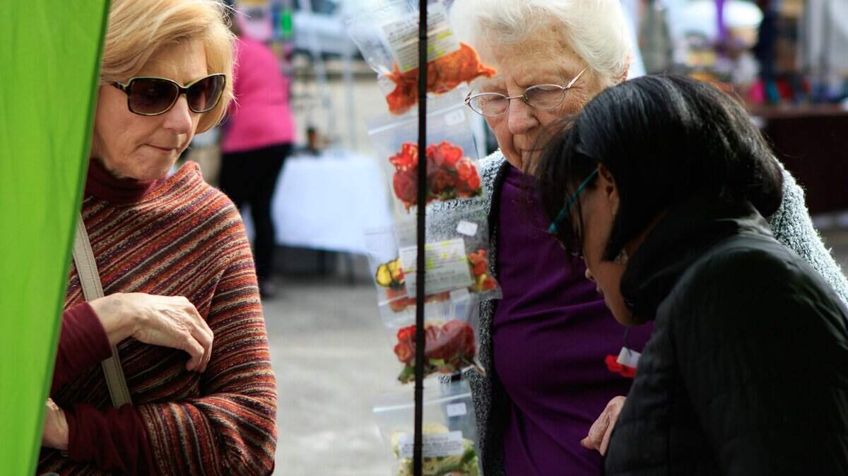 Carol Pitts (left) and Francis Pierce (center) listen as Kayla Strickland (right) describes the products her company, Ava's Apples, has for sale at the Downtown Open Air Market on Plum Street in November 2017.