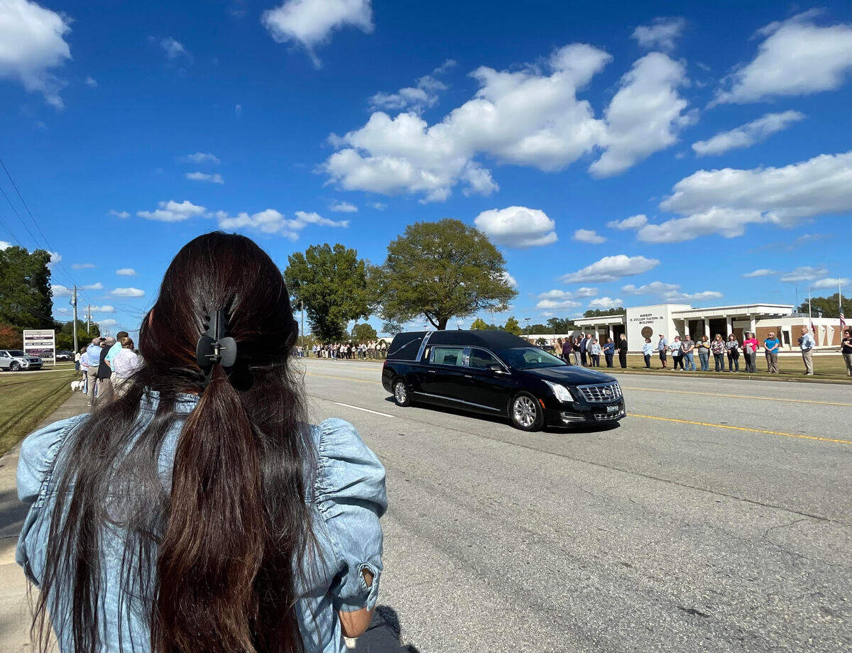 Susi Ortiz, left, stands in respect for the late Sheriff Cullen Talton, the nation’s longest serving sheriff, as a hearse carrying his body travels down Carl Vinson Parkway on Tuesday, Oct. 22, 2024.. The Sheriff H. Cullen Talton Jr. Building named after him is in the background.