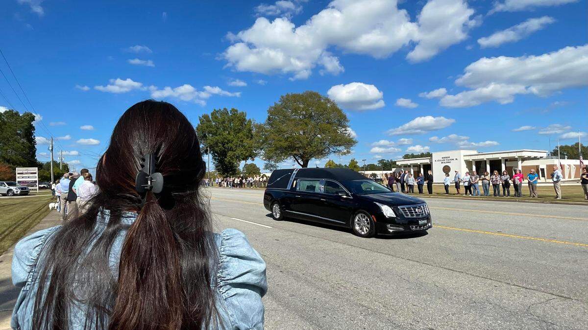Susi Ortiz, left, stands in respect for the late Sheriff Cullen Talton, the nation’s longest serving sheriff, as a hearse carrying his body travels down Carl Vinson Parkway on Tuesday, Oct. 22, 2024.. The Sheriff H. Cullen Talton Jr. Building named after him is in the background.