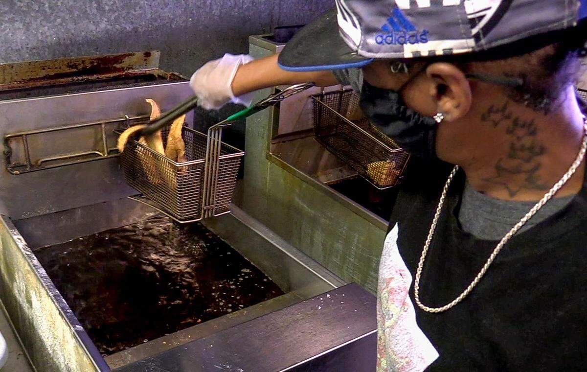 An employee removes a piece of whiting from a fryer at Saleem’s Fish Supreme.