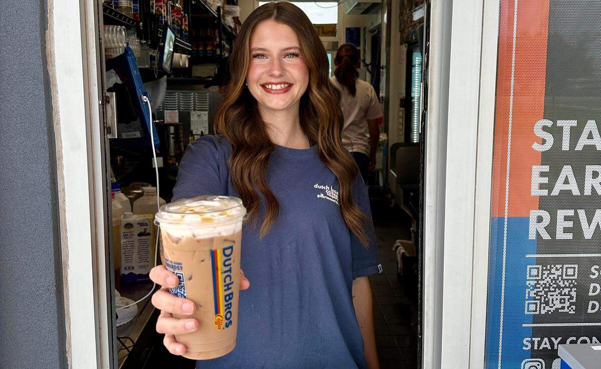 Maggie Briggs, the new regional operator for the Dutch Bros Coffee in Warner Robins, holds up her favorite “mafia style” iced “carmelizer” with a soft top and caramel drizzle at another store in Tulsa, Oklahoma.