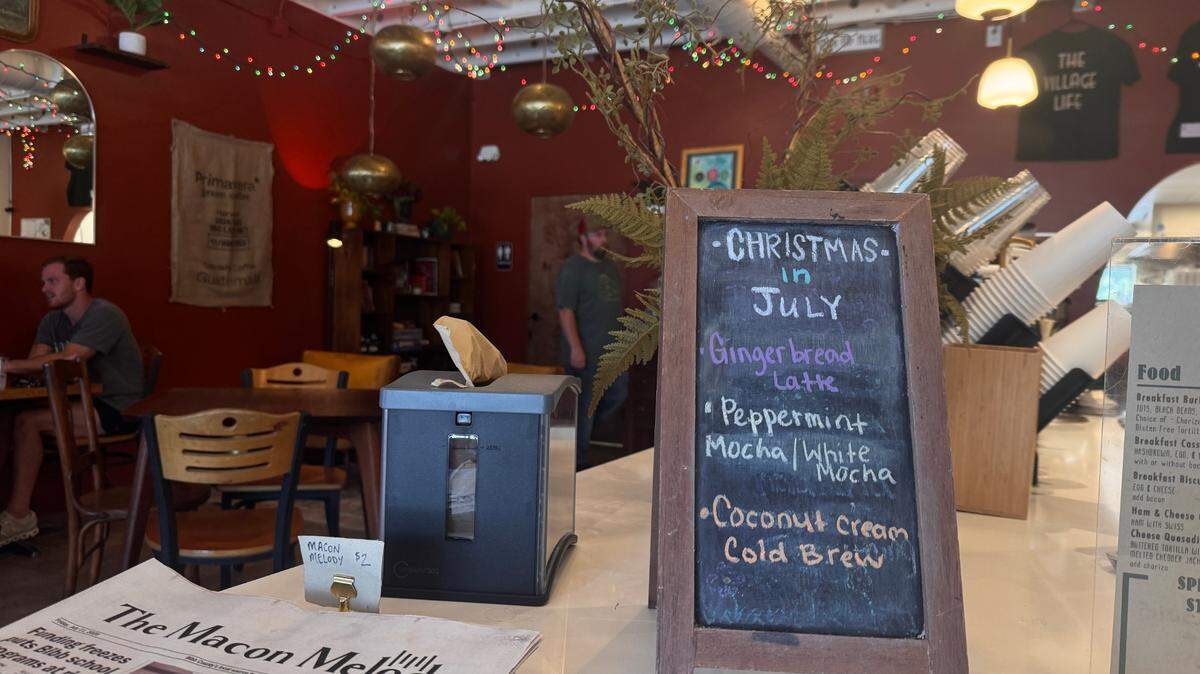 Christmas in July specials featured at Village Coffee on July 10th, 2025. Specials include gingerbread lattes, peppermint mochas, and peppermint white mochas. The cafe is decorated with Christmas lights to bring the holiday spirit in the hot, summer months.
