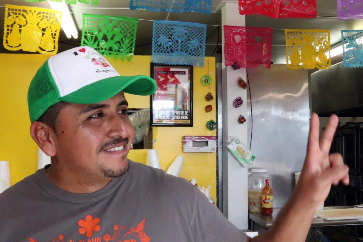 Adrian Saucedo-Luviano flashes a friend a peace sign at La Calentana, the bakery and takeout restaurant he owns and operates in Tifton. He is awaiting his date in immigration court after being arrested in Houston County. A sign behind the counter declares the premises an “ICE FREE ZONE.”