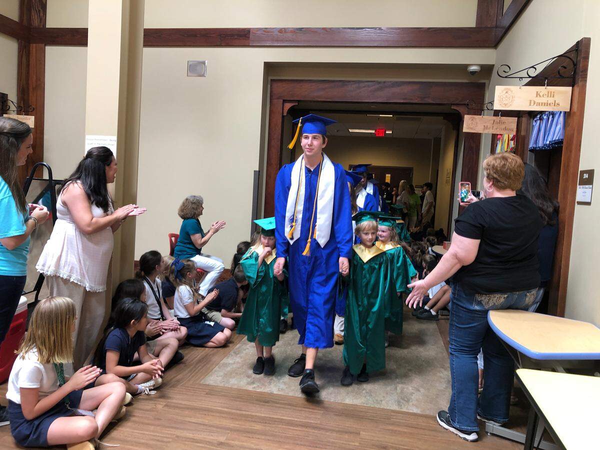 Andy Prather, a graduating senior at the Academy for Classical Education, holds hands of young scholars as he walks through the halls of the school a final time. Prater has attended ACE since leaving Miller Middle School in 8th grade. He is set to attend the University of Alabama this fall to study mechanical engineering.