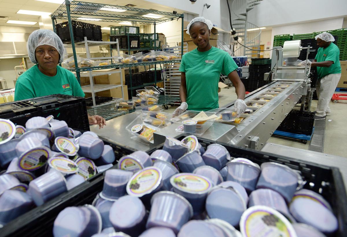 Candace Riggins, center, and other central kitchen workers assemble grab and go breakfast packages popular with Bibb County students.