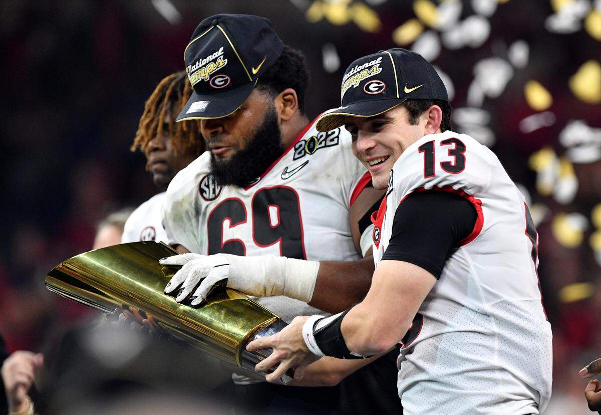 Georgia quarterback Stetson Bennett (13) and offensive lineman Jamaree Salyer (69) hold the championship trophy after the Bulldogs’ 33-18 win over Alabama in the College Football Playoff National Championship game Monday night.