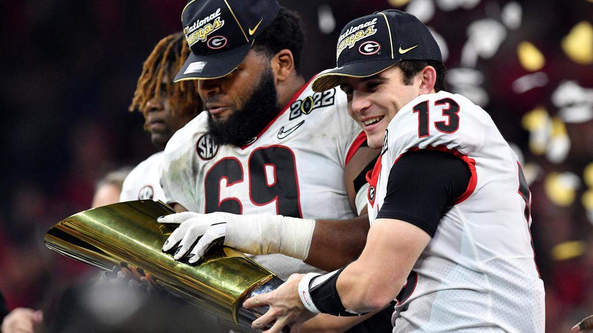 Georgia quarterback Stetson Bennett (13) and offensive lineman Jamaree Salyer (69) hold the championship trophy after the Bulldogs’ 33-18 win over Alabama in the College Football Playoff National Championship game Monday night.
