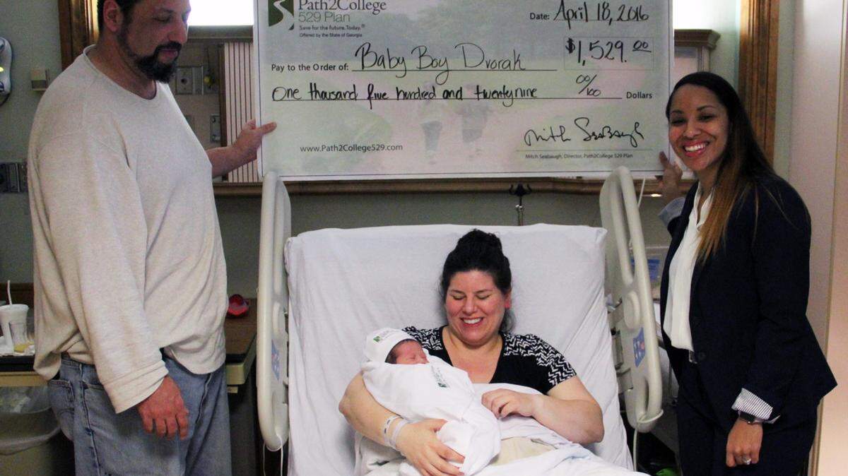 SPECIAL TO THE TELEGRAPH 
 Doron Dvorak, the baby's father, receives the gift from Path2College 529's Cassandra Sherrill, right, as mother Jacqueline Kennedy-Dvorak smiles at Baby Boy Dvorak.