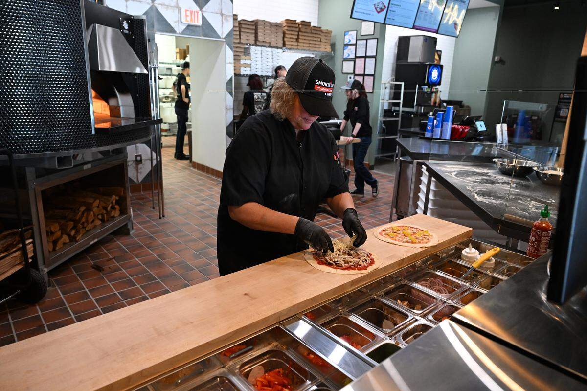 Smokin’ Oak Wood-Fired Pizza and Taproom chief operating officer Linda Black adds toppings to the Classic and Buffalo Chicken pizzas.