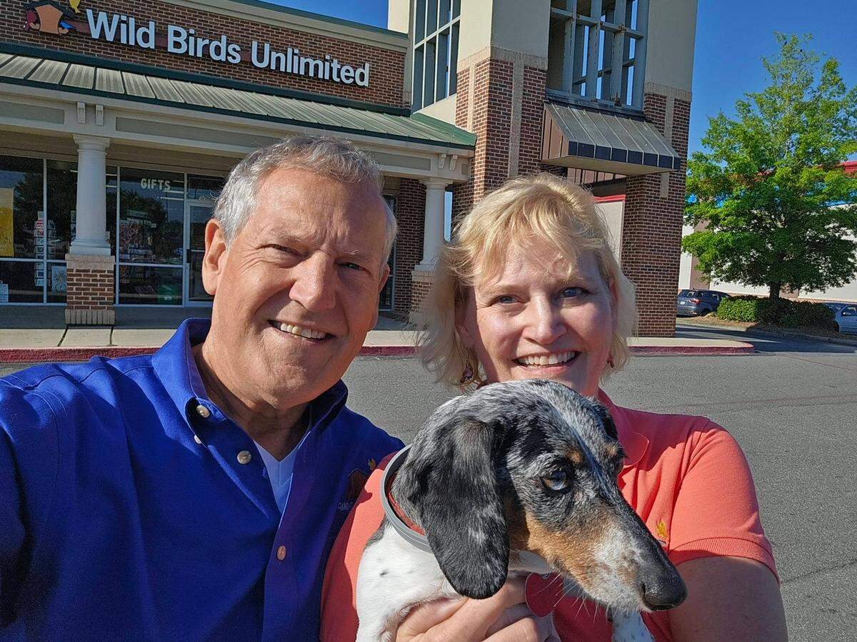 Wild Birds Unlimited owners David and Susan Van Houten smile for a photo on the store’s opening day with store mascot and greeter Duchess.