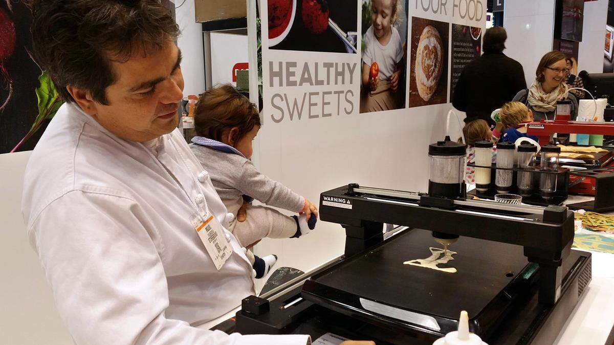 The PancakeBot show inventor Miguel Valenzuela demonstrates the pancake printer while holding his 5-month-old daughter, Charlotte, at the International Home + Housewares Show.