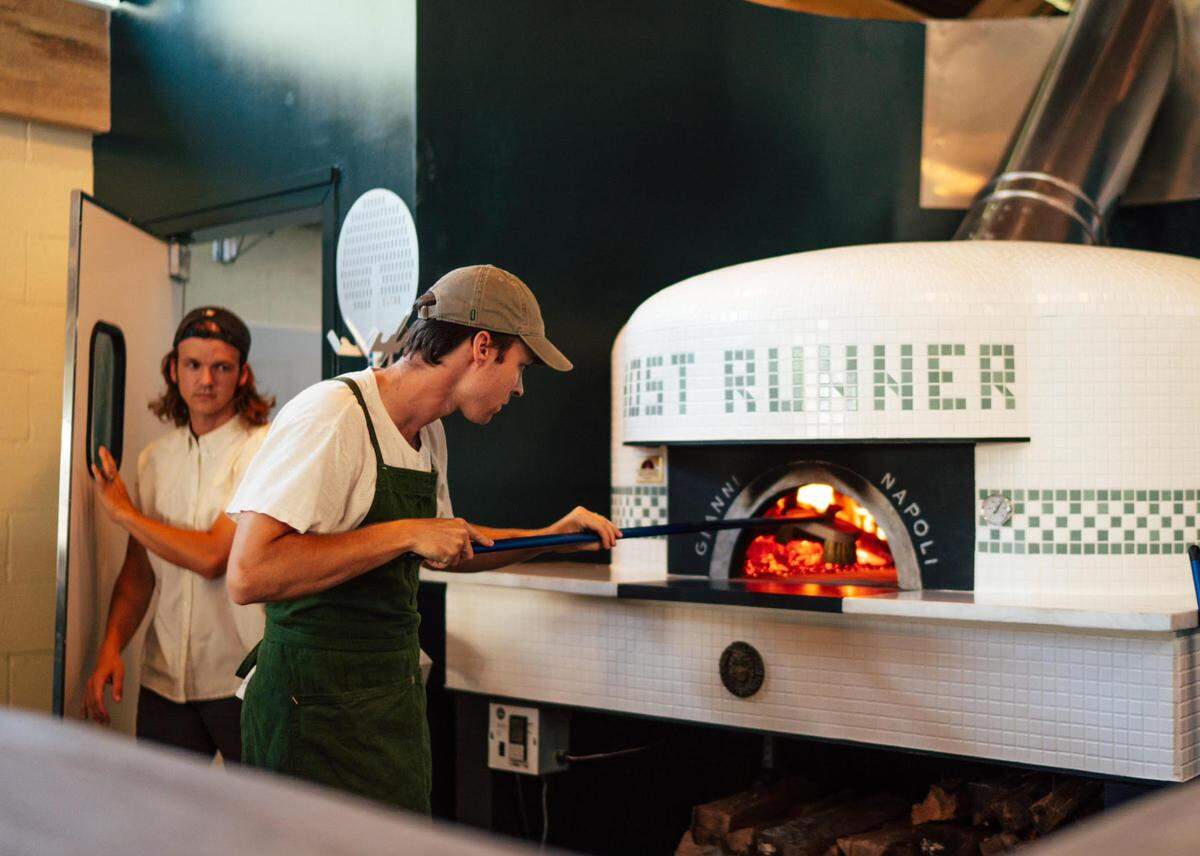 Wade Walker, co-owner of the new Ghost Runner Pizza spot in historic downtown Perry, tends the Fiero Forni wood-fired brick oven with gas assist, at a friends and family event prior to the restaurant opening. His brother and co-owner Cody Walker is pictured in the background.
