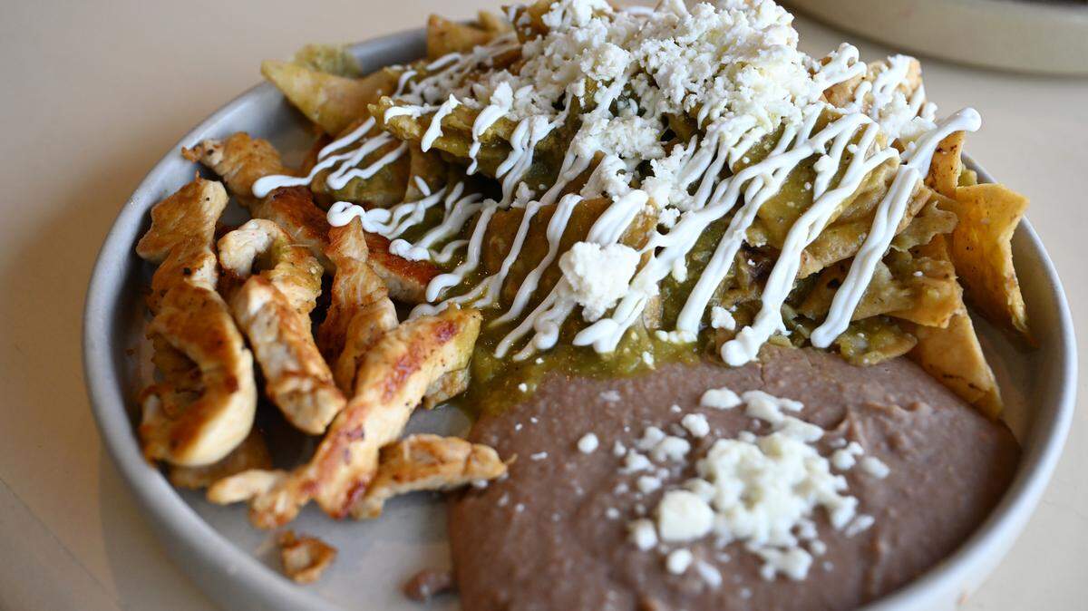 Green chilaquiles from Meridian Brunch & Bar, pictured with chicken, includes corn chips topped with salsa verde, sour cream, cheese and onions and comes served with refried beans. The brunch item includes the option of several proteins, including eggs or chorizo.