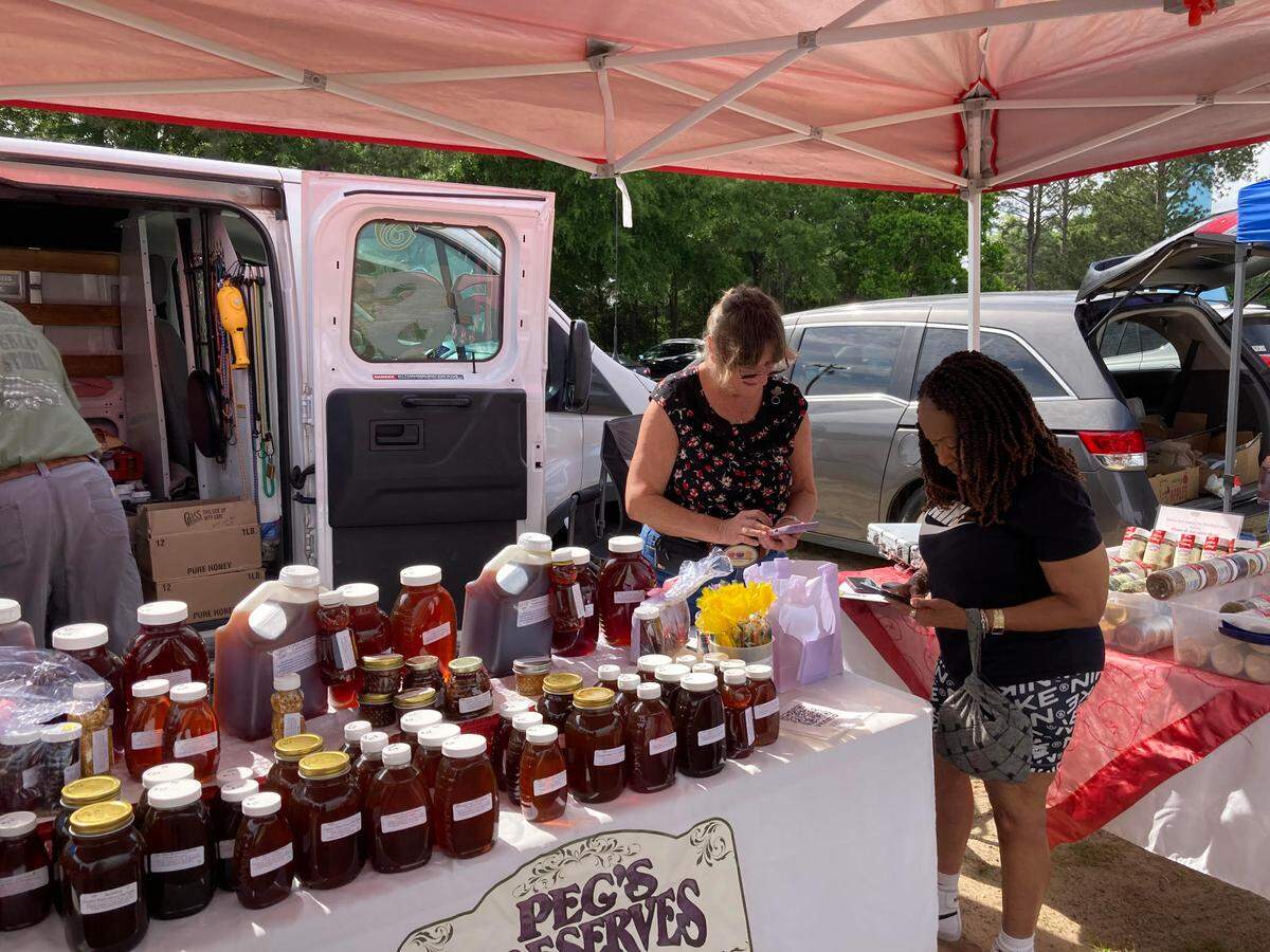 Peggy Corbett, owner of  Peg’s Preserves, corner right, with a customer at the International City Farmers Market in Warner Robins. Her booth includes a wide variety of homemade preserves, pickles and relishes, and honey from hives on her and her husband’s Byron orchard. He’s the bee keeper.