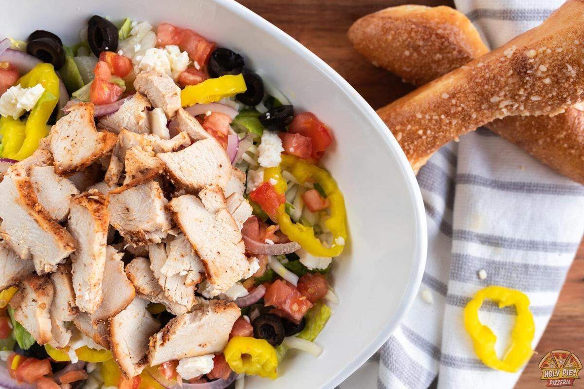 A Holy Pie! Pizzeria Greek salad with fresh-cut Romaine lettuce, black olives, cucumber, Feta cheese, banana pepper, tomato, red onion, topped with smoked chicken breast.