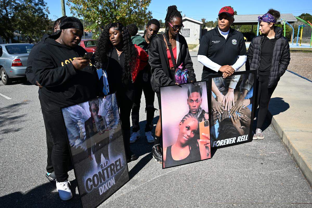 Family and friends of Contrel Dixon hold framed pictures of him while Shaquinta Card (left) reads remarks after a balloon release on Friday, Oct. 31, 2025, outside of the Rosa Jackson Recreational Center in Macon, Georgia. “I truly hope you’re at peace,” Card said about Dixon. “We love you forever.”