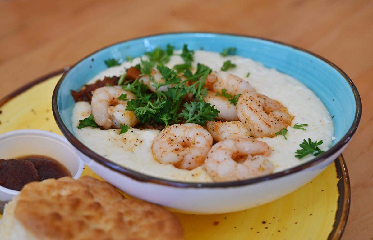The Award-Winning Shrimp & Creamy Dreamy Grits served with a Flying Biscuit sits on the counter at Flying Biscuit Cafe on Saturday, July 26, 2025, in downtown Macon, Georgia. The dish includes white cheddar grits with blackened shrimp and spicy marina sauce. 