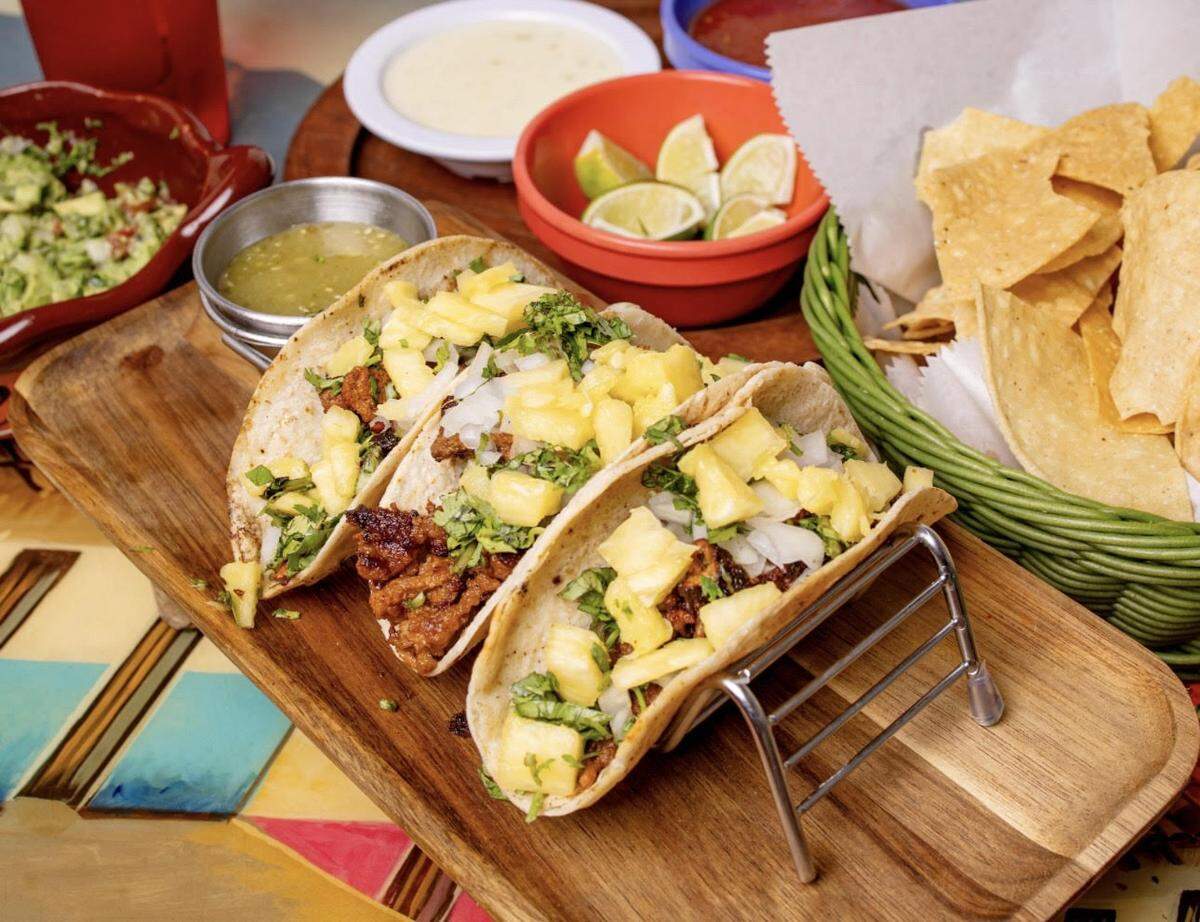 Tacos al pastor from El Metate Mexican Restaurant. Three tacos with marinated pork on soft corn flour tortillas with fresh onion cilantro and pineapple on top with green salsas. Served with a side of rice and beans.