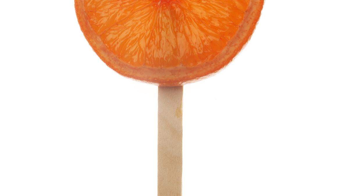 Negroni popsicle with the orange peel still on; the peel is removed to enjoy the cocktail popsicle.