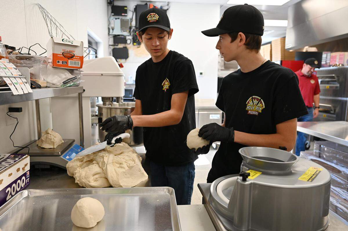 Brothers Brayden (left), 16, and Jackson Watson, 15, divide around 50 pounds of pizza dough into round sections in the new Holy Pie! Pizzeria in Perry, Georgia. The Watson brothers help out at their family’s business, which is operated by their dad Jake Watson Jr. and owned by their grandfather, Jake Watson Sr.
