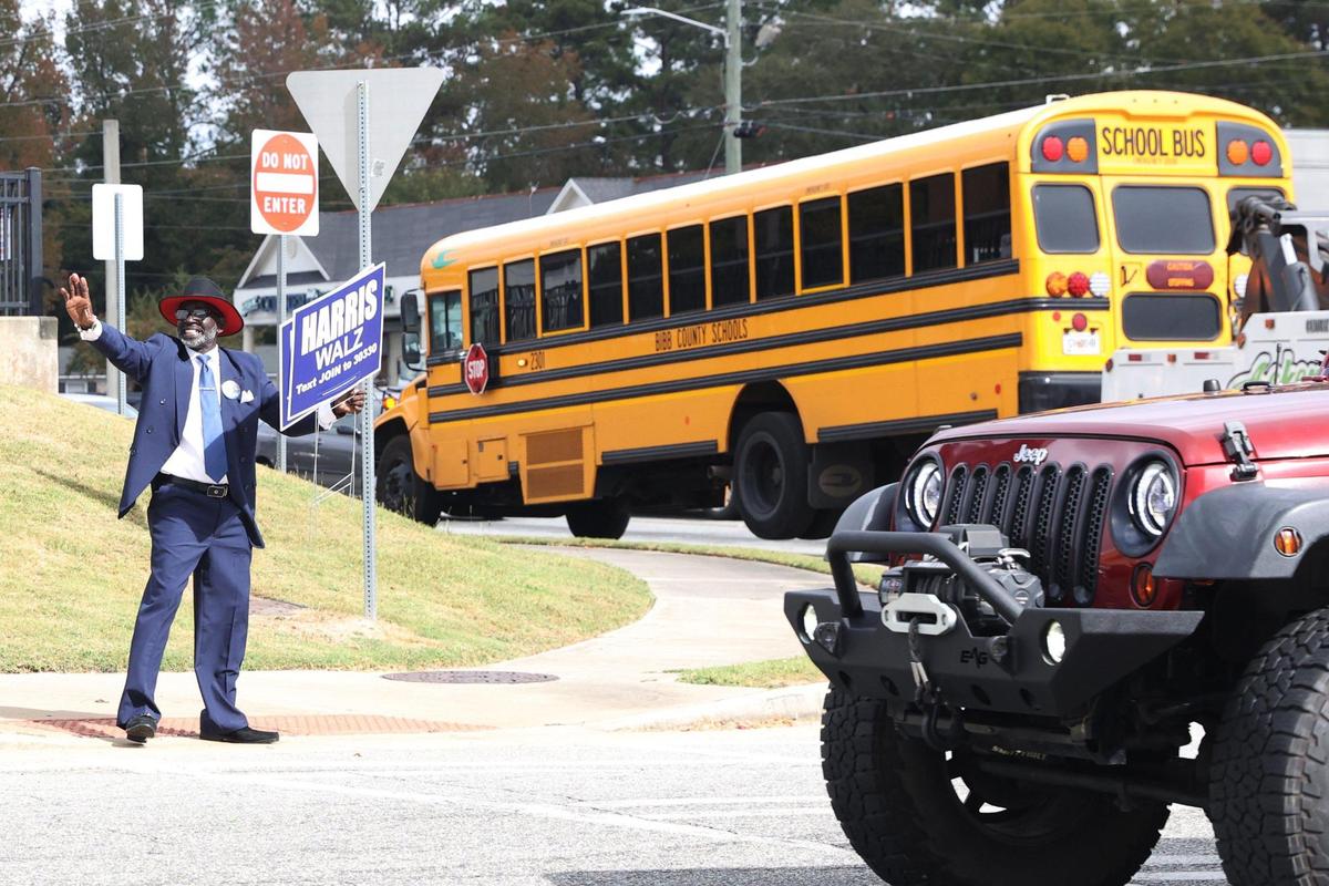 Carlton Kitchens waves while holding a sign for the Harris Walz presidential ticket at the intersection of Log Cabin Drive and Mercer University Drive on Election Day on Tuesday, Nov. 5, 2024, in Macon, Georgia. Kitchens stood on the corner waving signs for the Harris Walz presidential ticket for hours on Tuesday morning.