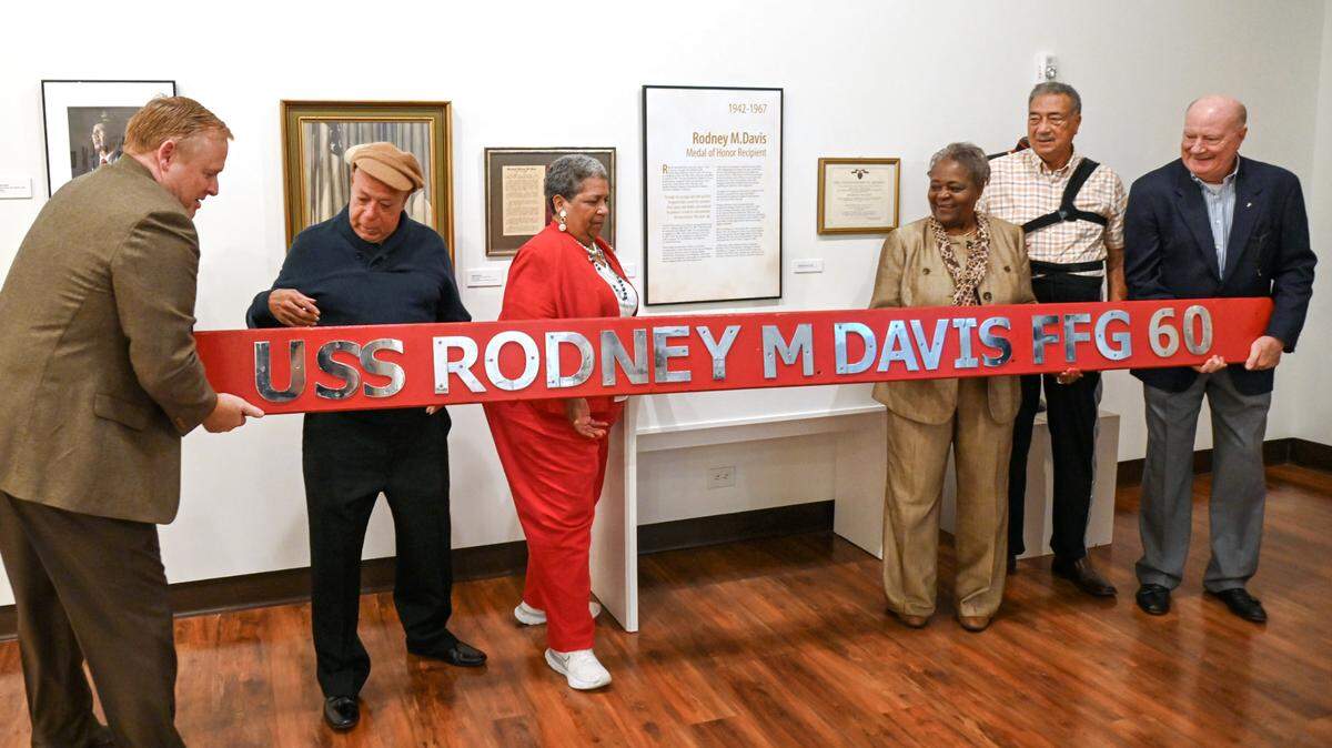Members of the 1/5 Vietnam Veterans group hold the nameplate from the USS Rodney M. Davis (FFG-60) as members of Davis’ family pose for a picture inside the Tubman Museum Thursday.