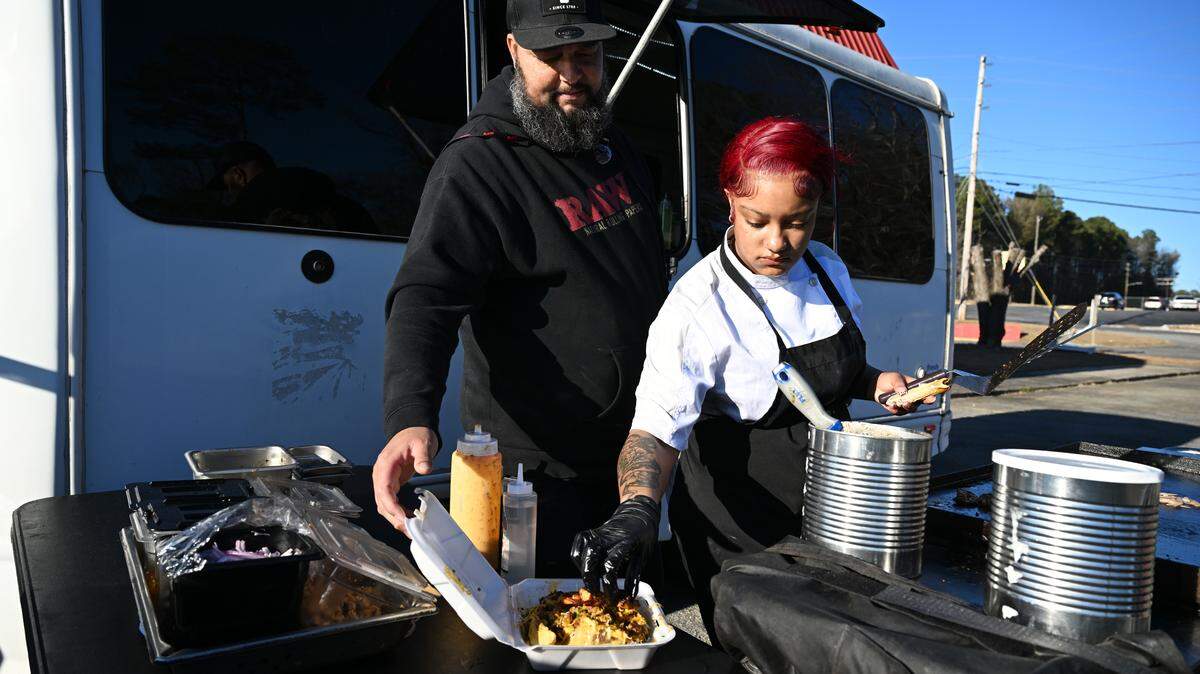 Phillip Hinson (left) grabs a loaded potato order while his daughter Jada Hinson, 21, plates outside of Hinson’s food truck on Friday, Feb. 6, 2026, in Shurling Plaza in Macon, Georgia. Hinson sells loaded baked potatoes from a food truck in East Macon and is working to re-open a physical restaurant.