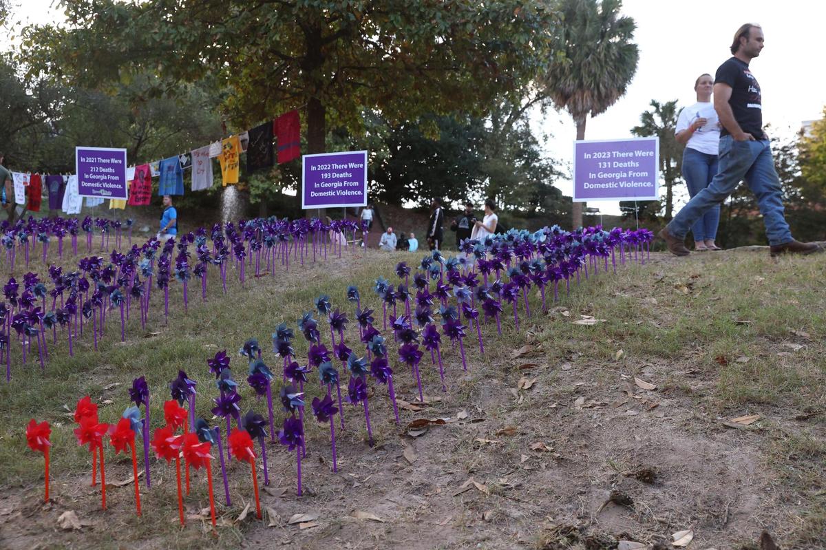 A vigil attendee walks by the pinwheel project as a part of the Domestic Violence Awareness Month candlelight vigil in Washington Square Park on Tuesday, Oct. 29, 2024, in Macon, Georgia. Each pinwheel represents one death from domestic violence in Georgia and the red pinwheels represent deaths in Middle Georgia.