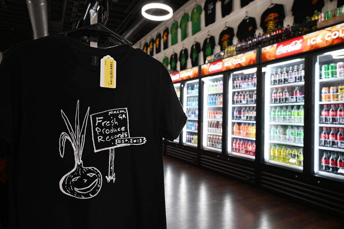 A Fresh Produce Records t-shirt sits inside of the new expanded storefront in front of a drinks cooler on Tuesday, Sept. 2, 2025, in downtown Macon, Georgia. The new side of the store features refrigerators with beverages for people to buy while browsing. 