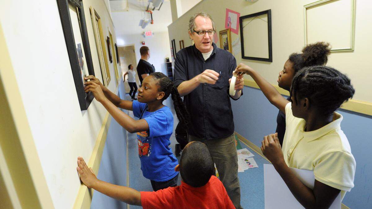 Mercer professor Creighton Rosental hands out tape to students in the Tindall Heights art program while hanging art at the Hester Bivins Youth Center Friday afternoon. The program started by Rosental and run by Mercer students displayed the students art during an open house Saturday.