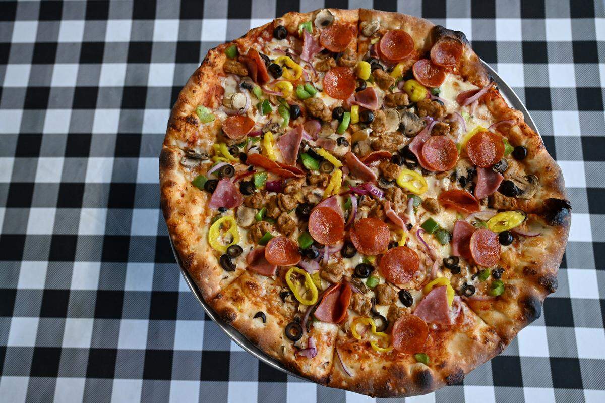 A large "The Home Slice" pizza sits on a table in Home Slice Pizza on Tuesday, Aug. 26, 2025, in Perry, Georgia. The pizza features pepperoni, ham and sausage with a variety of vegetables.