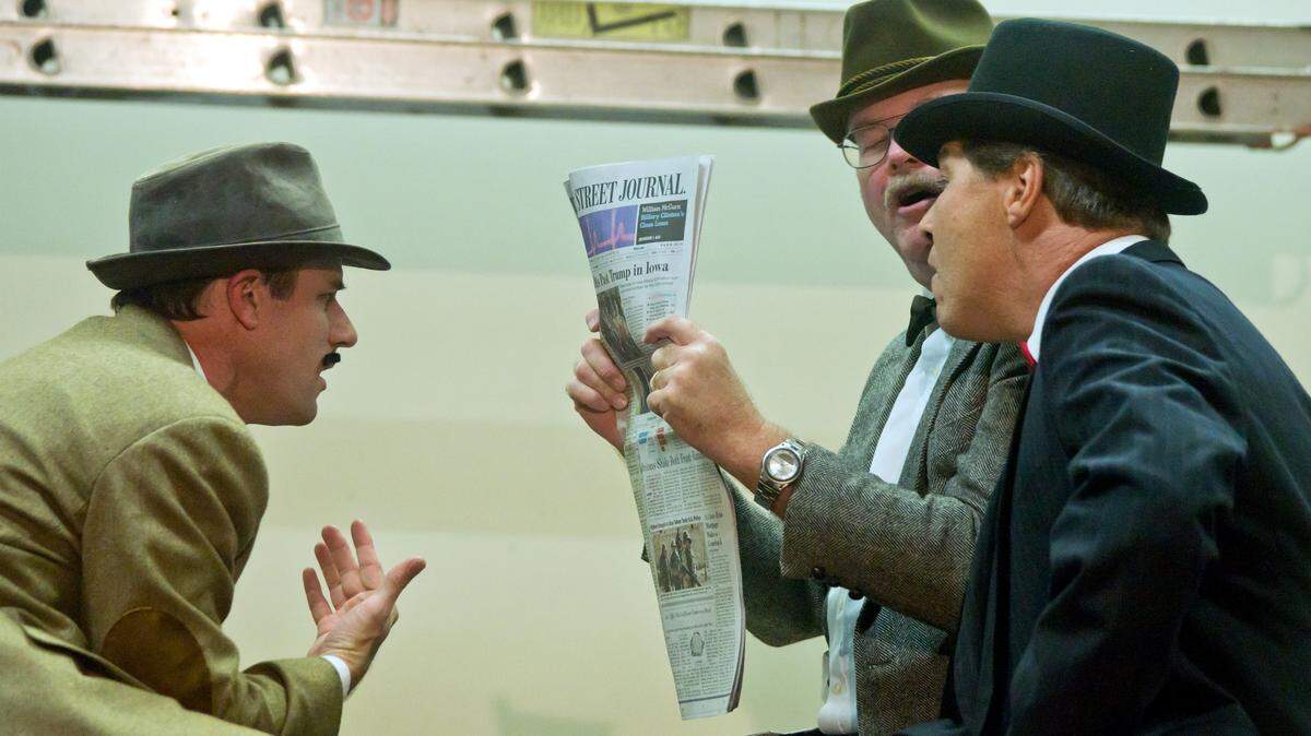 Jason Niederkorn, left, as Richard Hannay, reads a story in another passenger's newspaper that names him as a murder suspect.  The other Flying Scotsman passengers are Todd Wilson and Bill Johansen.