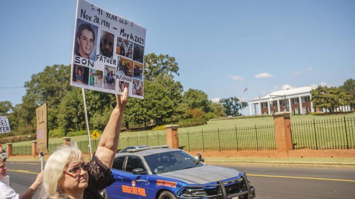Carrie Proffitt protests in 2023 across from the Georgia Governor’s Mansion with photos of her son who took his own life in a Georgia Department of Corrections prison.
