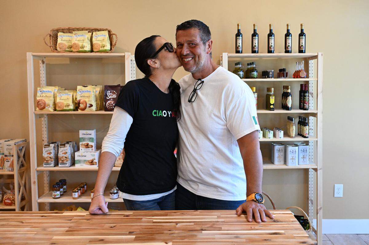 Husband and wife owners Telisa (left) and Daniele Asaro pose inside of their new business, Ciao Bella Market in downtown Perry, as Telisa sneaks in a kiss.