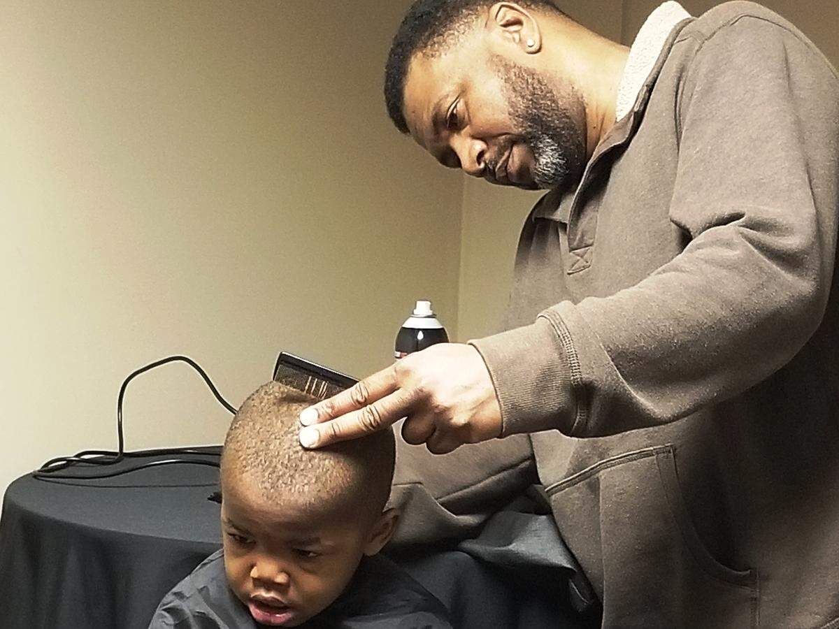 Leroy Jarrell, co-owner of Just Right Barber Shop in Macon, gives Deshon Glover, 3, a hair cut Tuesday during the Anita Ponder and Friends Christmas Feast held at Terminal Station in Macon on Christmas Day.