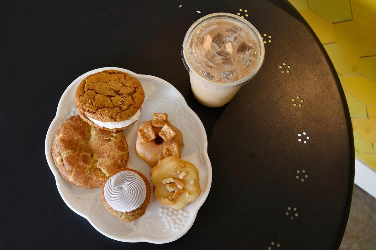 A gluten free vegan oatmeal crème pie, snickerdoodle, Cinnamon Toast Crunch donut, banana pudding donut and earl grey cupcake sit on a plate inside of Oh Honey Baking Co. with an iced honey bee latte on Thursday, May 23, 2024, in Macon, Georgia.
