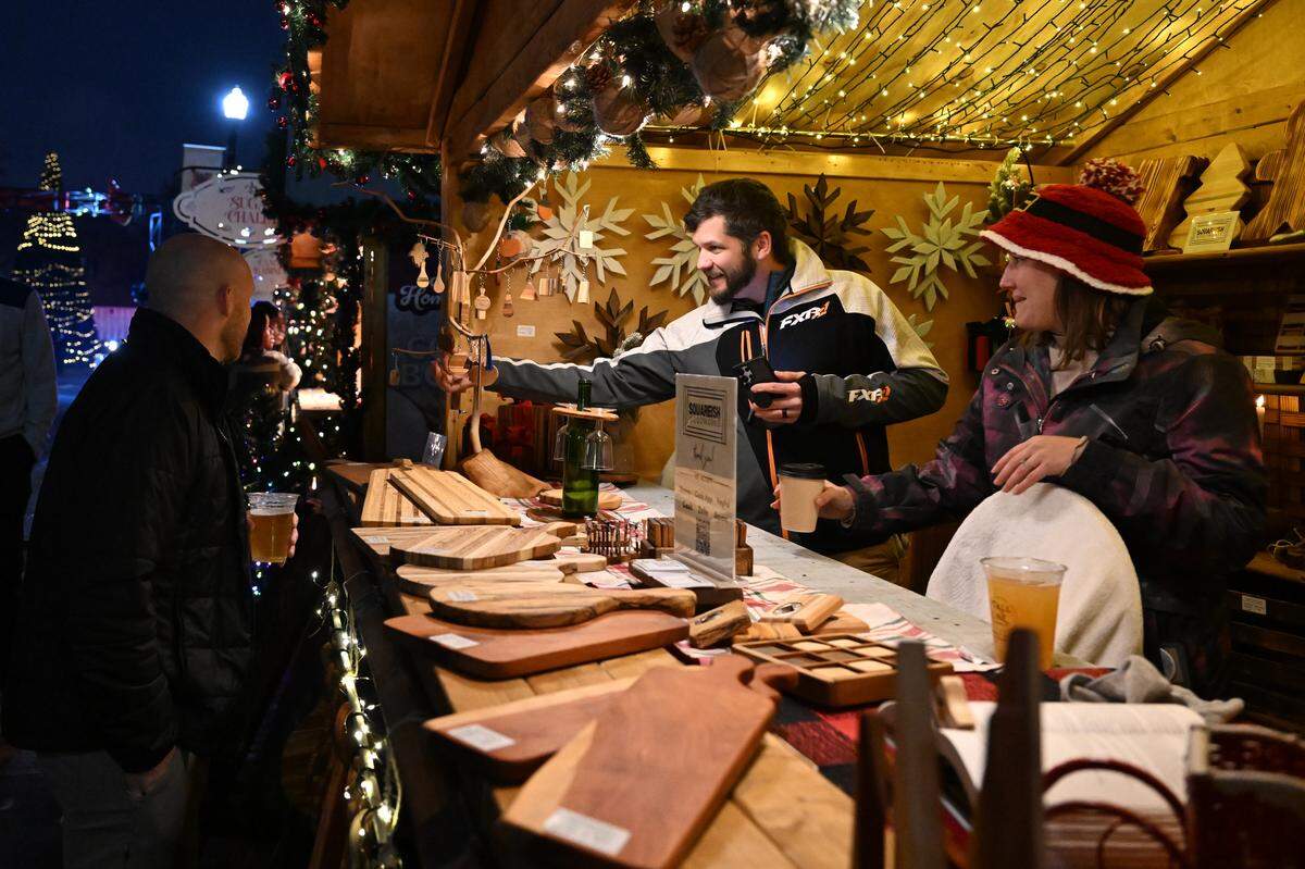 Squareish Woodworks owner Billy Copeland, right, and his wife, Ashley Copeland, from Milledgeville, speak to customers from their booth at the Marchè de Noel during a preview on Thursday, Dec. 4, 2025, in downtown Macon. The inaugural Macon Christmas Market is modeled after a traditional European Christmas market and features a number of small business vendors.