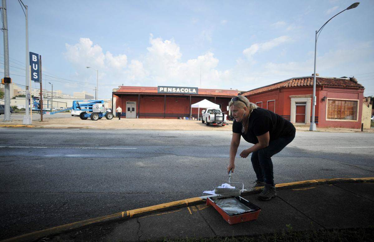 Tammy Trimble paints a curb gray along Third Street in front of a shop that was being fashioned as the Pensacola, Florida, bus terminal for the movie “42” in this June 14, 2012, file photo.
