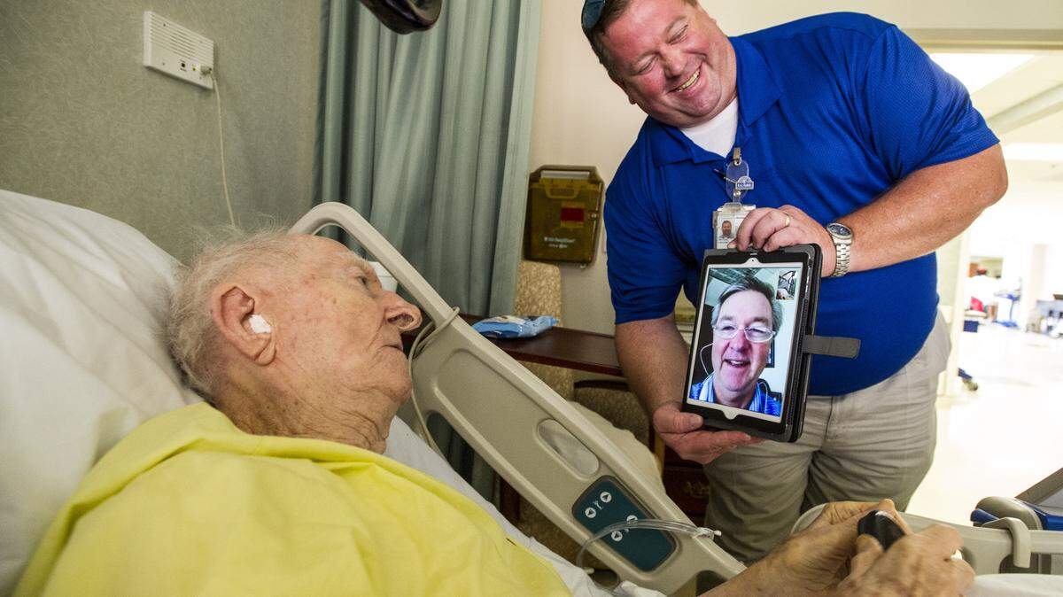 Social worker Greg Senters holds an iPad as World War II veteran Newell NeSmith speaks with his son Al NeSmith in Atlanta from his bed in the Carl Vinson VA Medical Center in Dublin on Thursday morning.