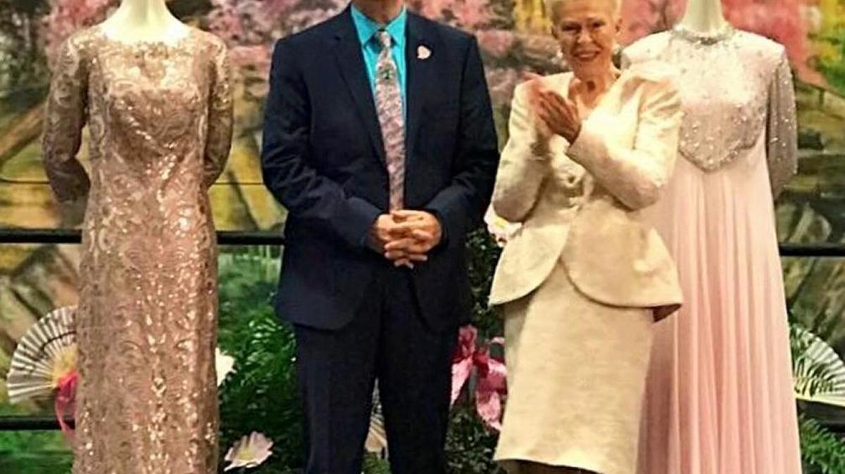Mark Ballard stands with Carolyn Crayton at the Cherry Blossom Festival Fashion Show on March 30. Behind Crayton is the gown she wore to the festival ball 35 years ago, and behind Ballard is the gown she wore to this year’s ball.