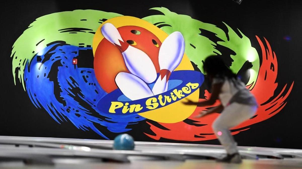 Asiyah Spratley, 6, rolls a bowling ball at Pin Strikes in front of a large mural painted by Angie Henigman and her brother Daniel Henigman.