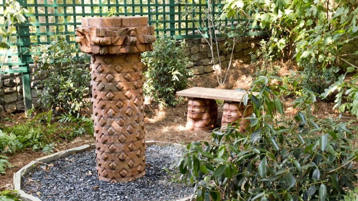 In a secret garden, Tanner Coleman’s sculptures, Column I, and a pair of gargoyles support a garden bench at the Macon home of Stephen Reichert.