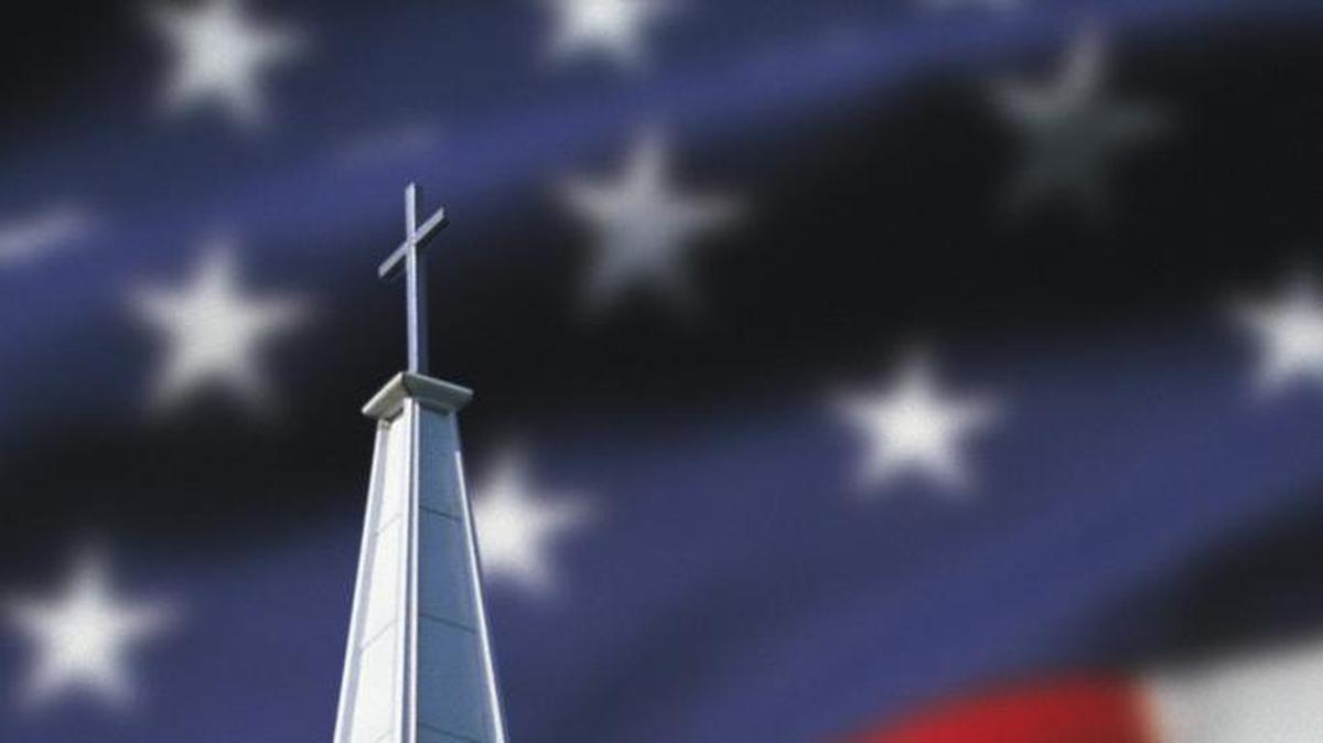 A church steeple in front of an American flag.