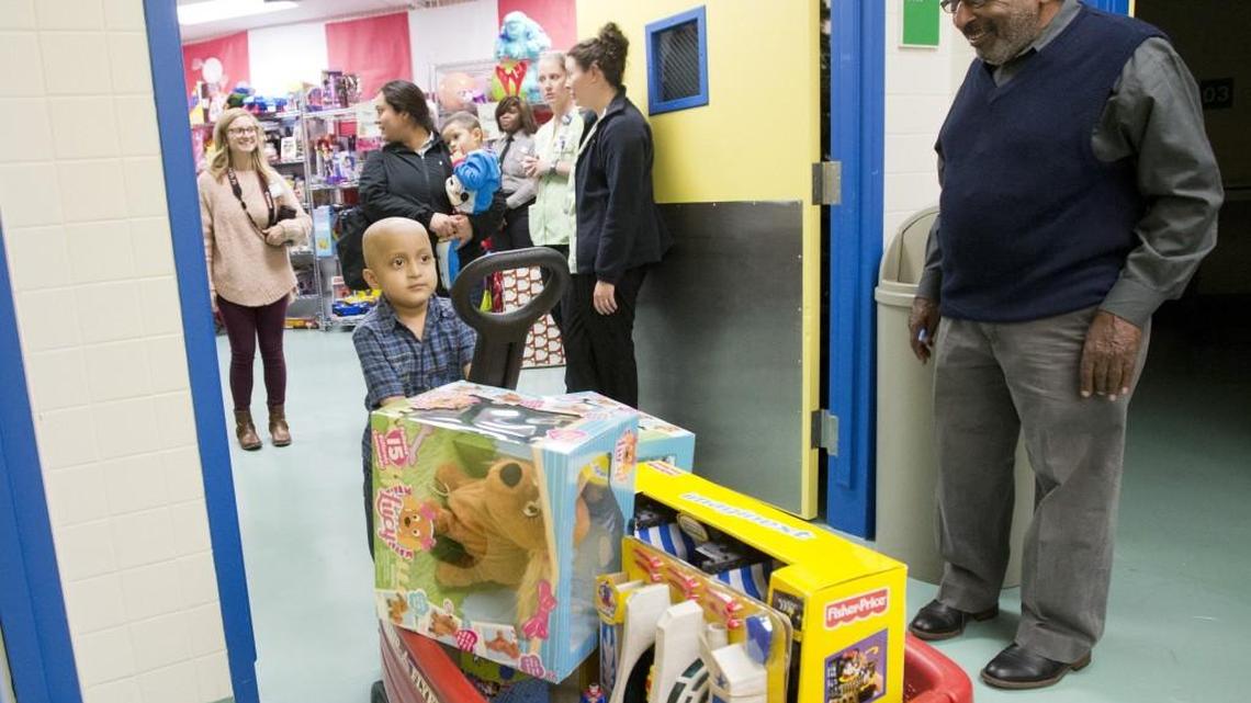 Larry Villa, 4, a patient at Children’s Hospital, Navicent Health, wheels out a section of toys for himself and his siblings from the hospital's Holly Jolly Shoppe on Dec. 6, 2016. Walter Timley, who helped launch the tradition 12 years ago, smiles in the doorway.