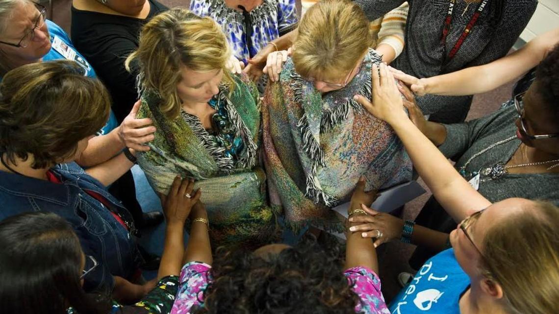 Wendy Wood, left, and Shannon Grieshop stand in the middle of a prayer circle Wednesday. The two Hilltop Elementary School teachers, surrounded by teachers and paraprofessionals, have hands laid on them as they are prayed for at a meeting of the Teachers Living for Christ after school. Grieshop will be received a kidney from Wood Thursday at Emory in Atlanta.