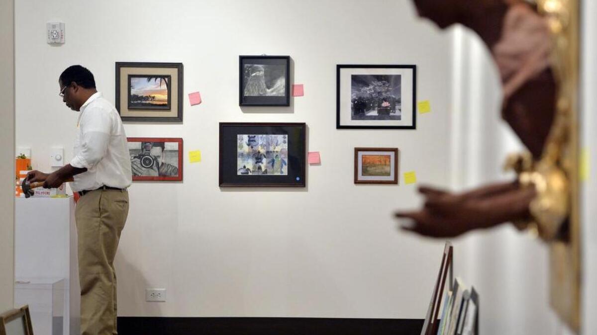 Tubman Museum Director of Exhibitions Jeffrey Bruce hangs paintings, photos and mixed media works Nov. 3. Nore than 130 pieces by Bibb County school district employees or relatives will be featuring in the new National Arts Program exhibit.