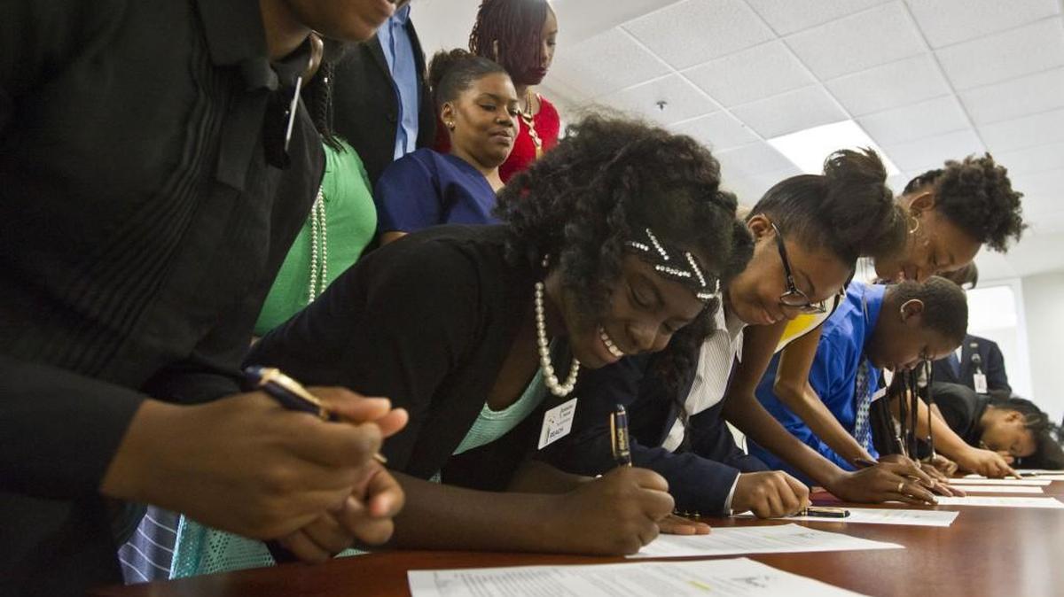 Eight REACH scholars from Appling Middle and Ballard-Hudson Middle schools sign the contract during the ceremony. The students and their families signed contracts to uphold program requirements, that include maintaining a 2.5 grade point average through high school and staying out of trouble with the law. If they do they will receive a $10,000 scholarship for college.