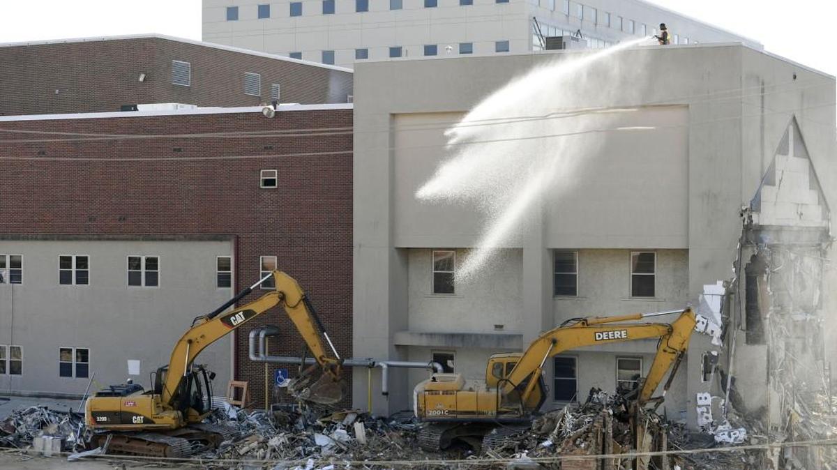 A member of the demolition team sprays water on debris below to keep the dust down as two excavator operators load the the razed building into trucks and containers in this March 22 file photo. The Children's Hospital, Navicent Health, is being removed to make way for a new building for the unit.